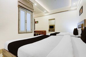 A hotel room with two beds, a window with curtains, a small table, a sofa, and a wall-mounted TV. - Collection O Sachivalaya Metro Station (Gandhinagar)