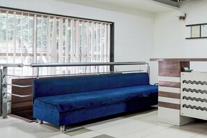 Una habitación con un sofá azul, una baranda de metal y una ventana con persianas verticales.