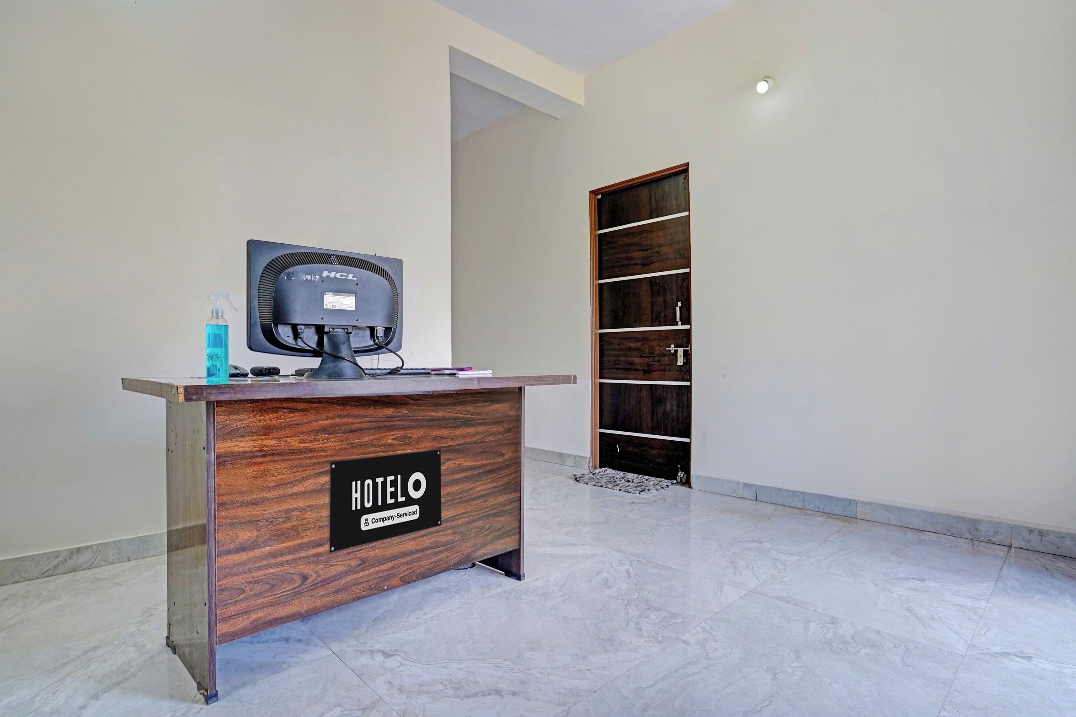 Una recepción con un cartel que dice 'HOTELO Company Serviced' en un interior moderno con suelo de mármol y una puerta de madera al fondo.