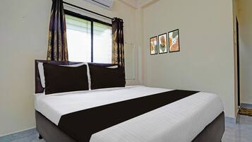 A hotel room with a bed, curtains, an air conditioning unit, and two framed artworks on the wall.