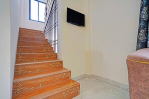 A staircase with ornate wood detailing, a black television mounted on the wall, and a patterned curtain.