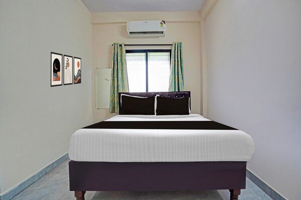 A bedroom with a bed, an air conditioner, a window with curtains, and wall art.