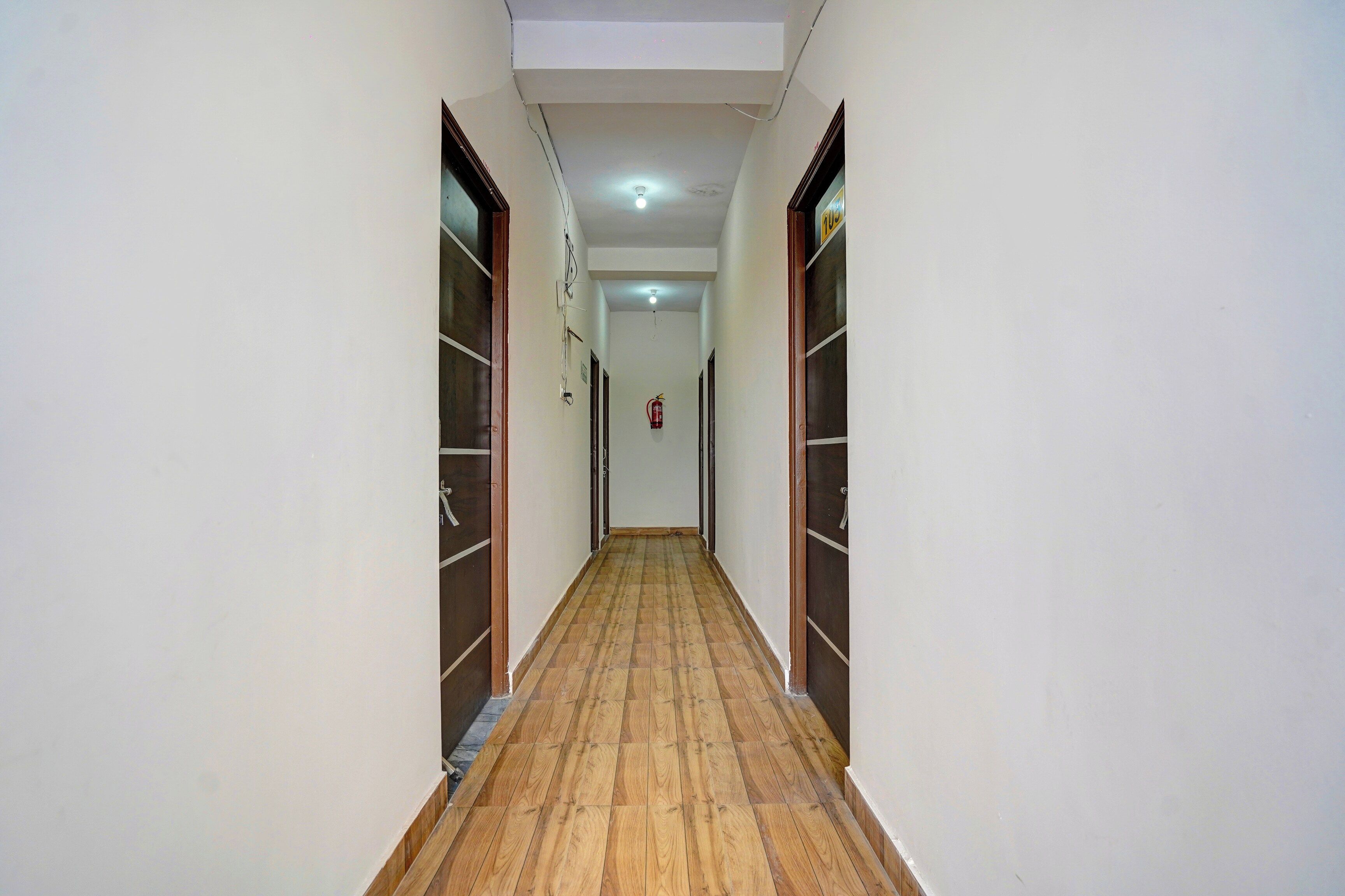 Un pasillo con suelo de madera, paredes blancas y puertas a ambos lados.