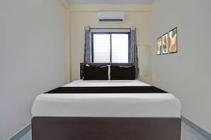 Ein Hotelzimmer mit Bett, Klimaanlage, einem Fenster mit Vorhängen und Wandbildern.