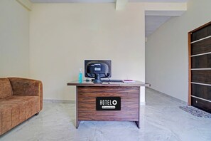 Mostrador de recepción de hotel con monitor de computadora, una botella de agua y un letrero que indica que la habitación cuenta con servicio de empresa.