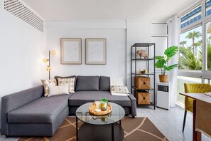 A modern living room with a grey sectional sofa, a glass coffee table, and a black bookshelf. - Al Andalus Torremolinos – Bright Coastal Apartment near La Carihuela, Restaurants & Centre (Torremolinos)