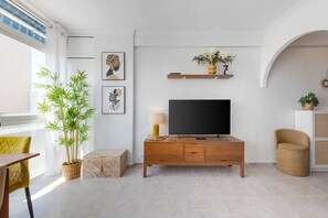 Una sala moderna con televisor de pantalla plana, un mueble de madera, una planta en maceta y un sillón amarillo.