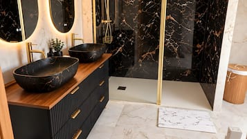 Een moderne badkamer met een zwart marmeren wastafelmeubel, gouden details en een douche met glazen wanden.