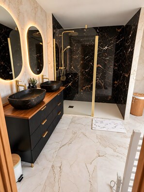 Ein modernes Badezimmer mit Waschtisch aus schwarzem Marmor, goldenen Armaturen und einer Duschkabine.