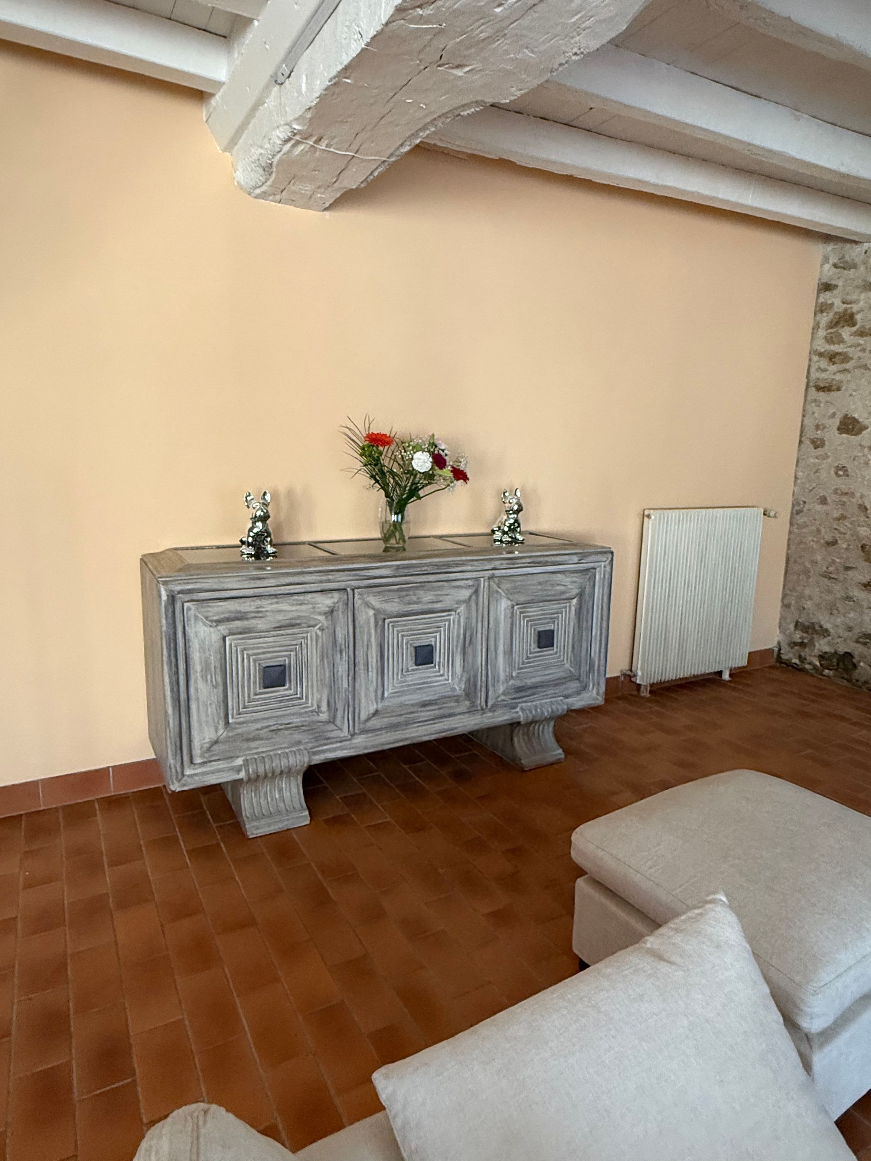 Una habitación con un mueble grande y decorativo en una pared, un radiador y suelo de baldosas.