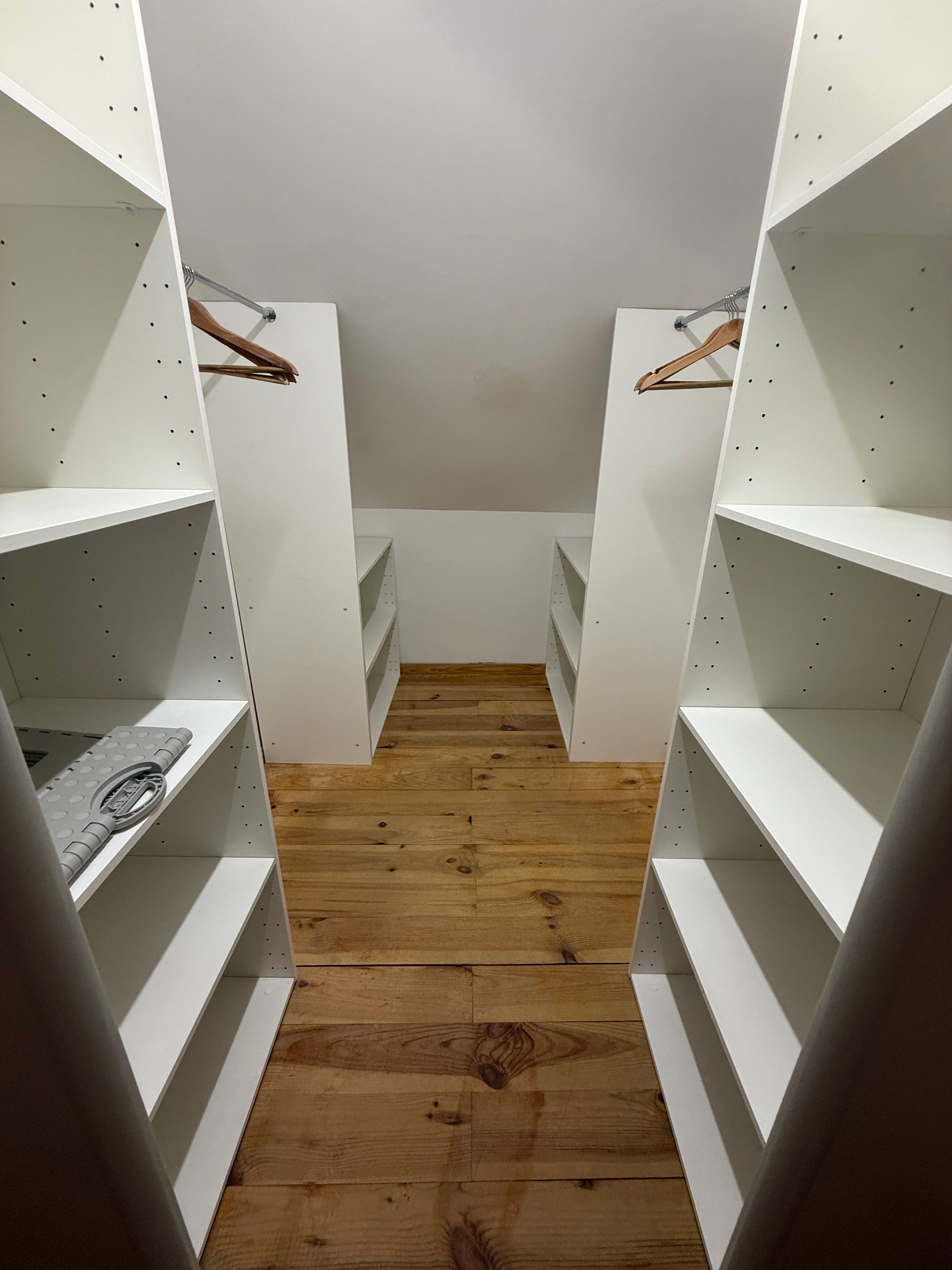 Ein schmaler Durchgangschrank mit weißen Regalen und Holzboden.
