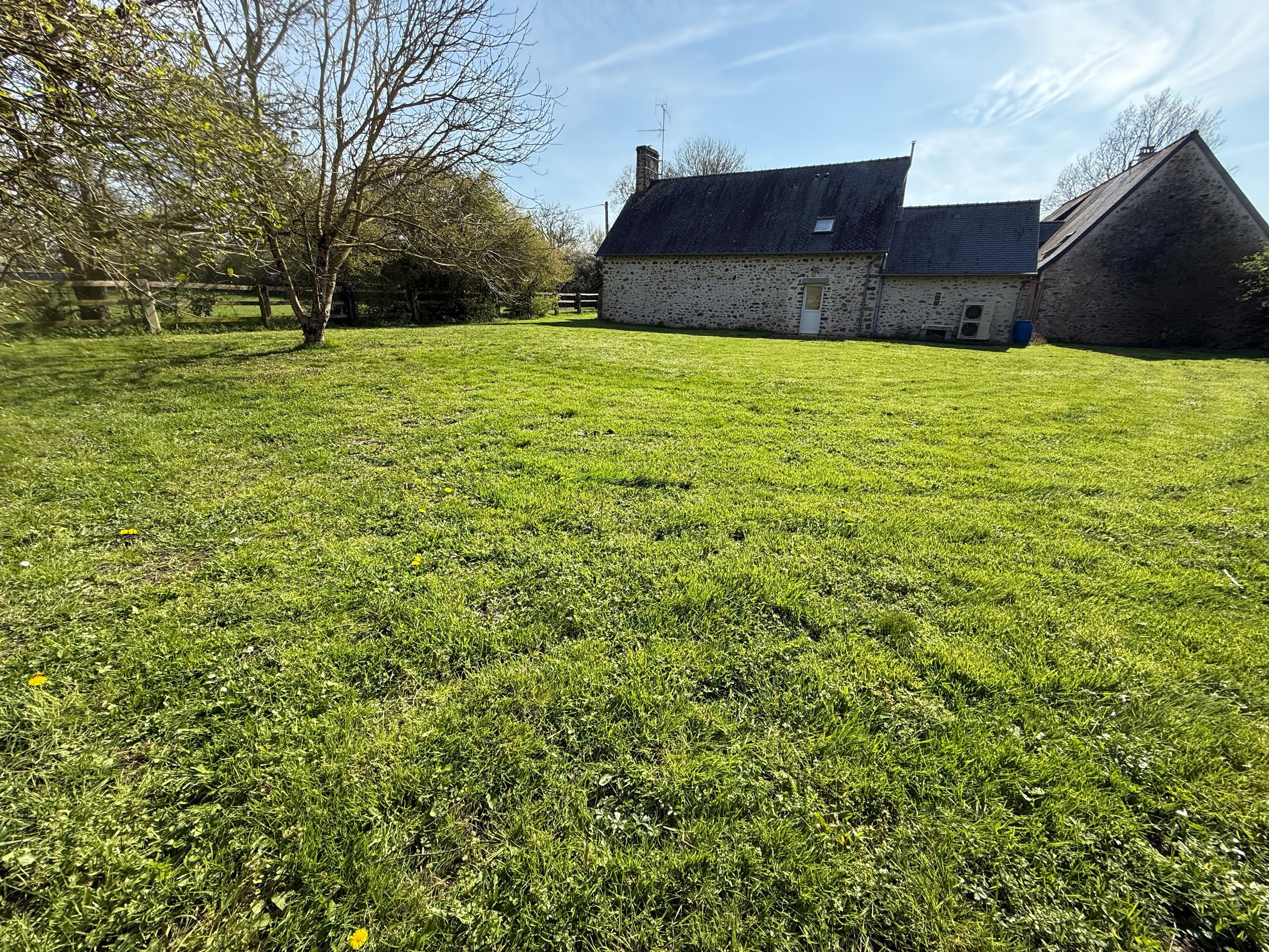 Un champ herbeux avec un bâtiment en pierre et un arbre.