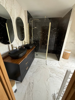 Ein modernes Badezimmer mit einem schwarzen Marmor-Waschtisch, zwei Waschbecken, einem großen Spiegel und einer Duschkabine.