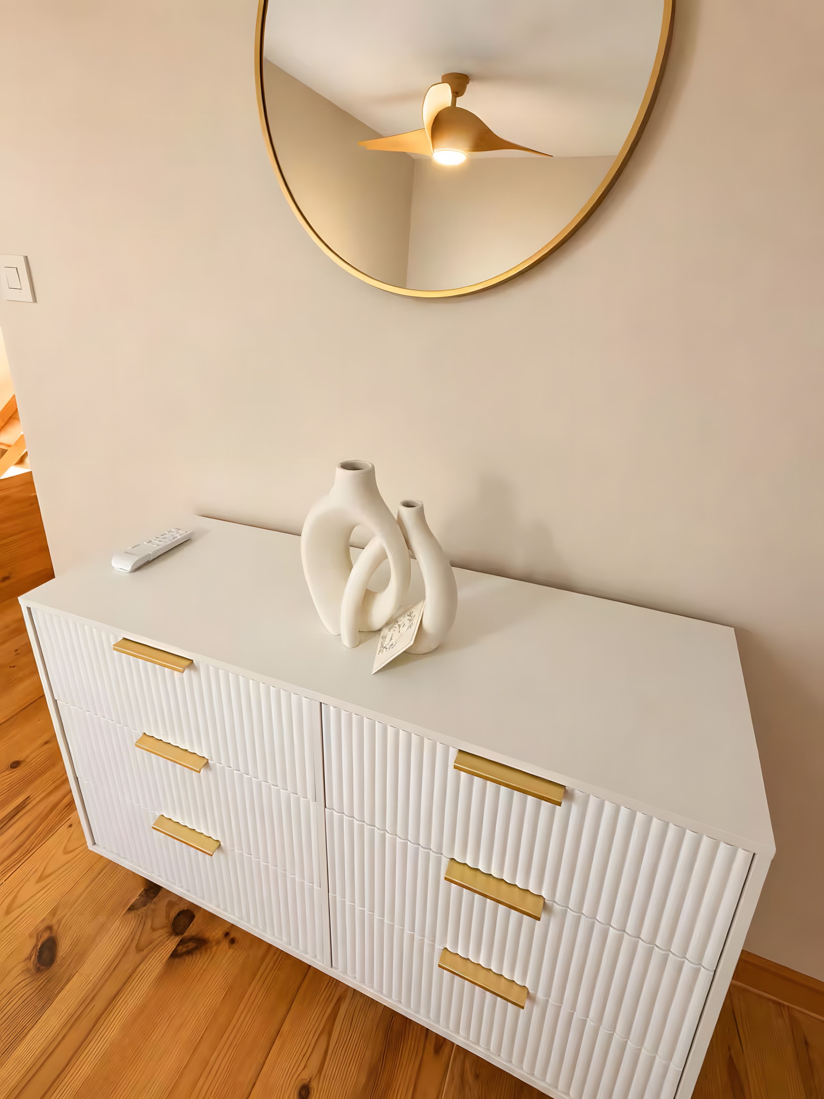 Un meuble blanc avec des poignées dorées, sur lequel est posé un vase blanc.