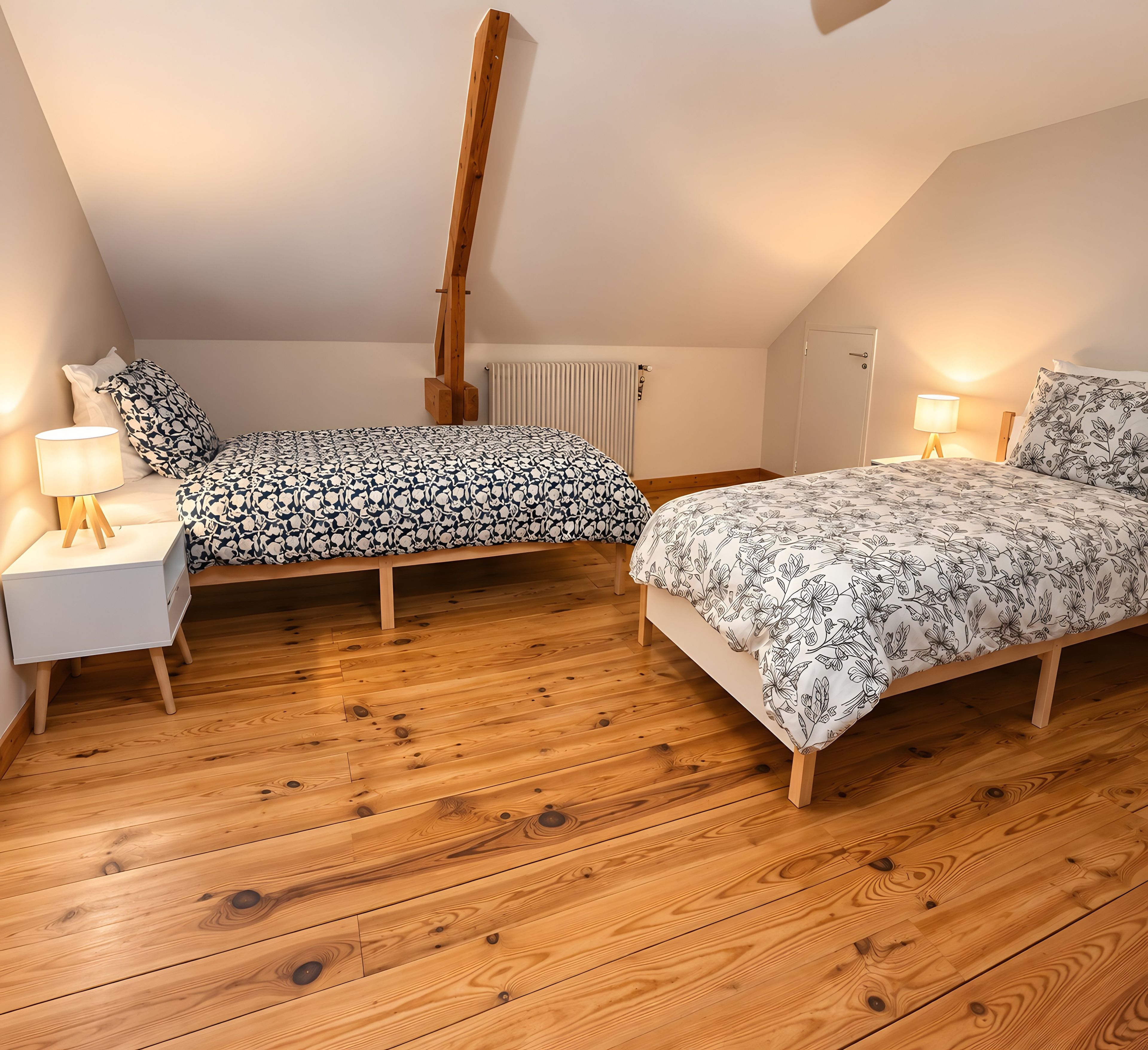 Een slaapkamer met twee bedden, houten vloeren, een radiator en bedlampjes.