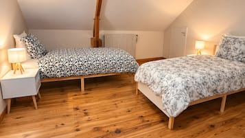 Een slaapkamer met twee bedden, houten vloeren, een radiator en bedlampjes.