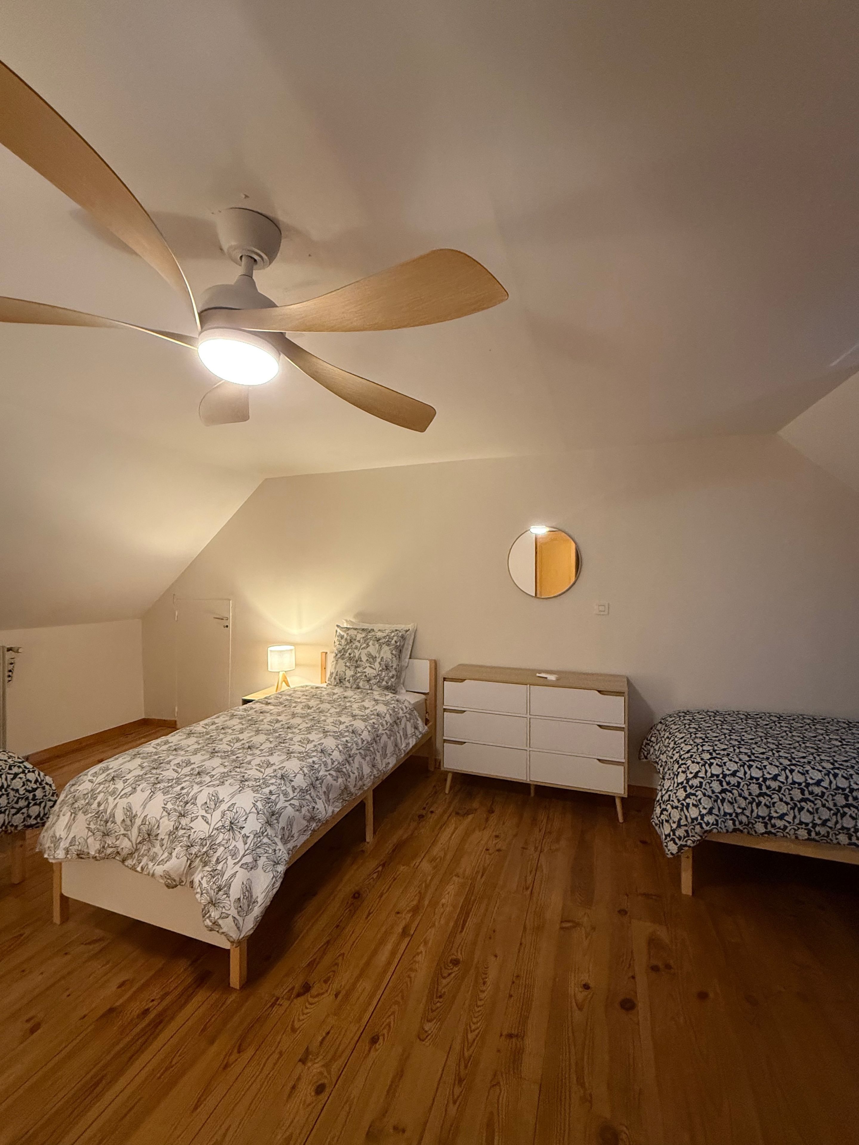 Ein Schlafzimmer mit Deckenventilator, einem Bett mit floralem Bettbezug, einem Nachttisch mit Lampe und einer Kommode.