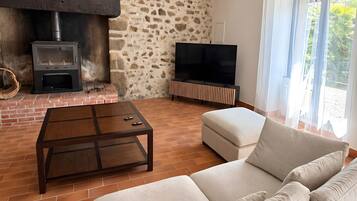 Un salon avec un mur en pierre, une cheminée, un téléviseur et un canapé.