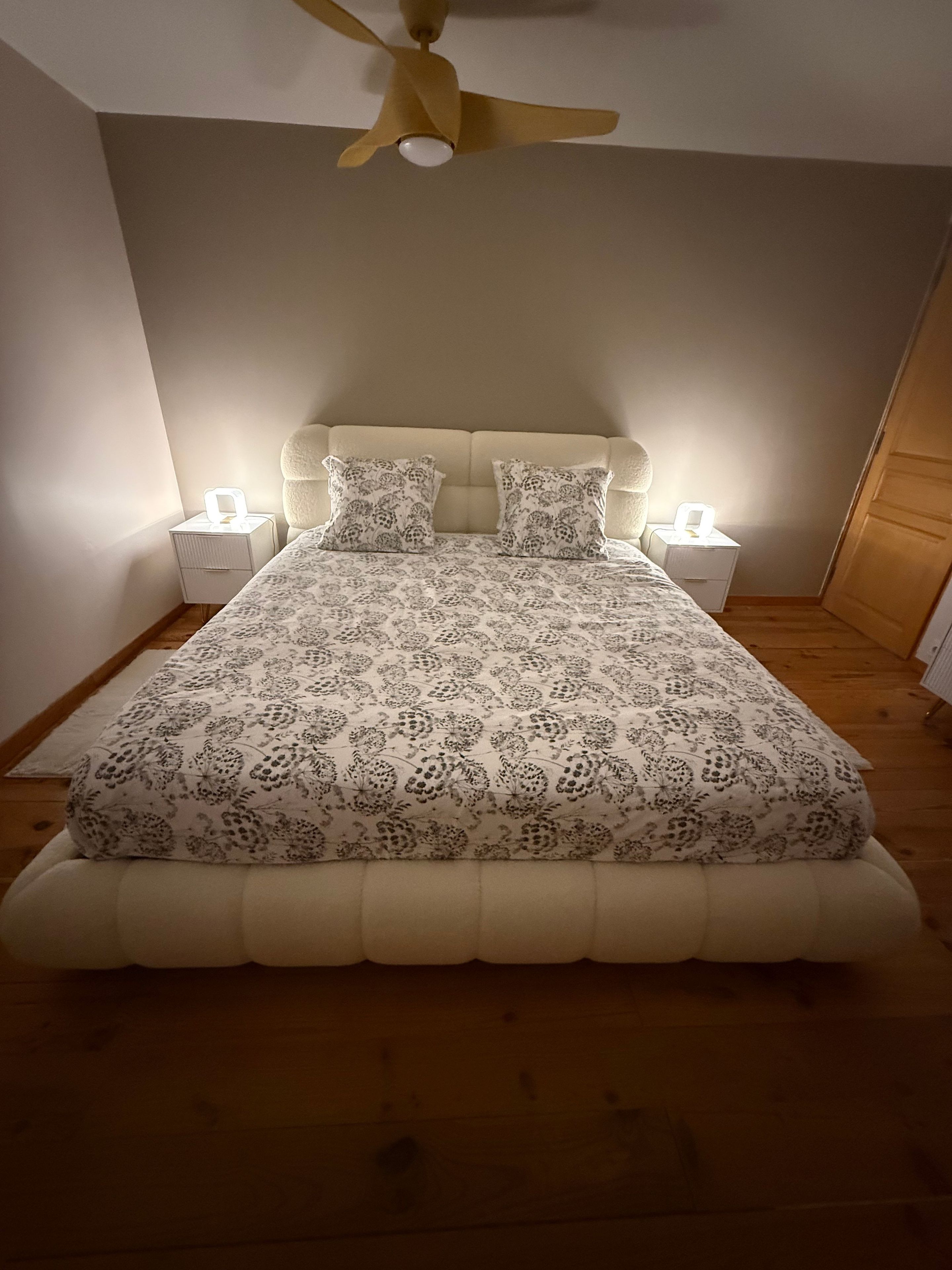 Ein Schlafzimmer mit einem Bett, Deckenventilator, Nachttischen und einem Beistelltisch.