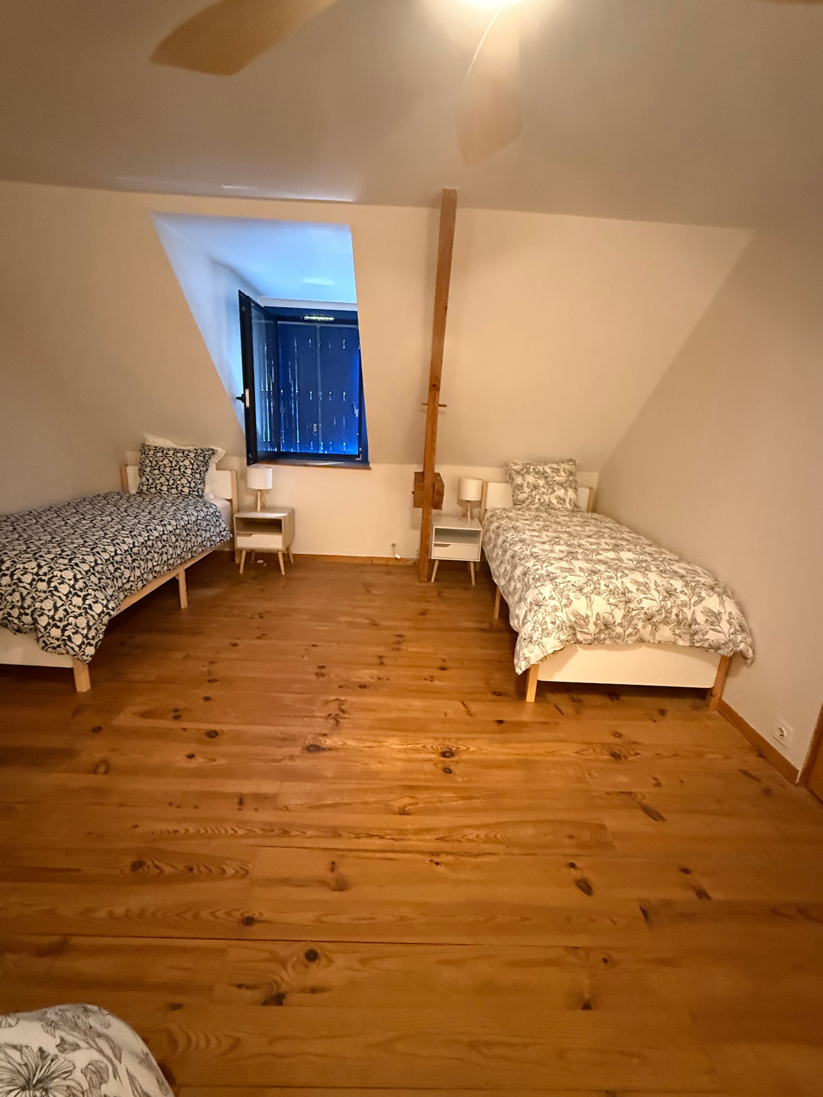 Een kamer met twee bedden, een klein bureau, een stoel en een raam met uitzicht op het exterieur.