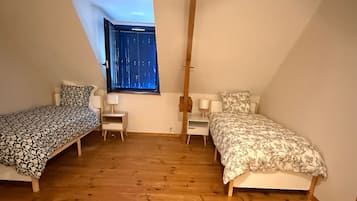 Een kamer met twee bedden, een klein bureau, een stoel en een raam met uitzicht op het exterieur.