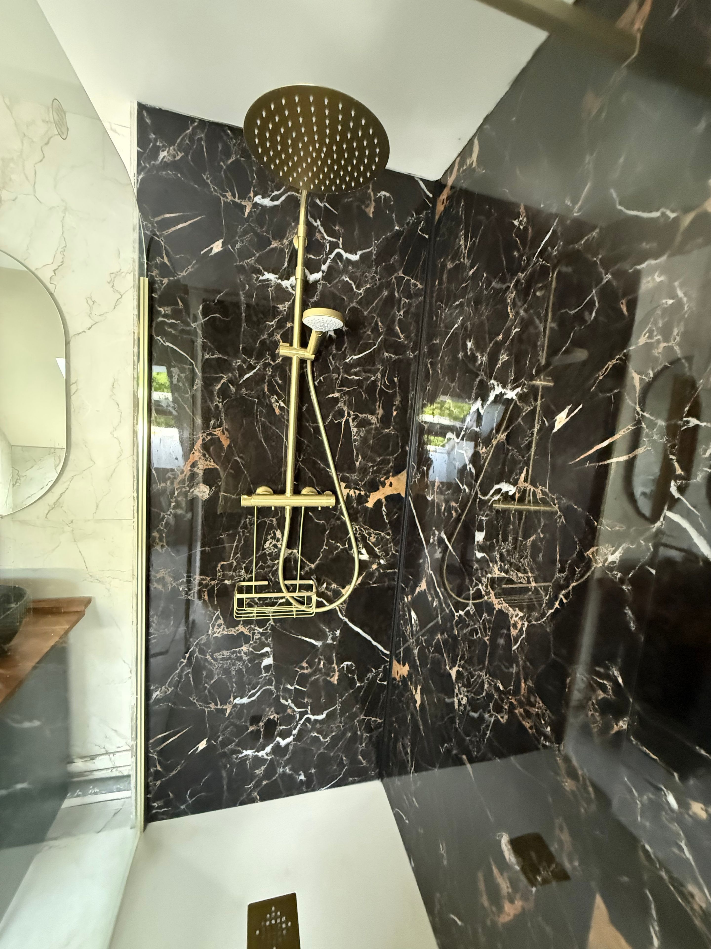 Een badkamer met een wand van zwart marmer, een gouden douchekop en een gouden kraan.