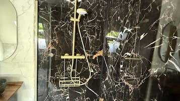 Een badkamer met een wand van zwart marmer, een gouden douchekop en een gouden kraan.