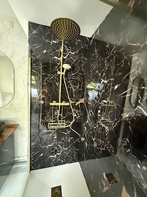 Ein Badezimmer mit schwarzer Marmorwand, goldener Duschbrause und goldenem Wasserhahn.