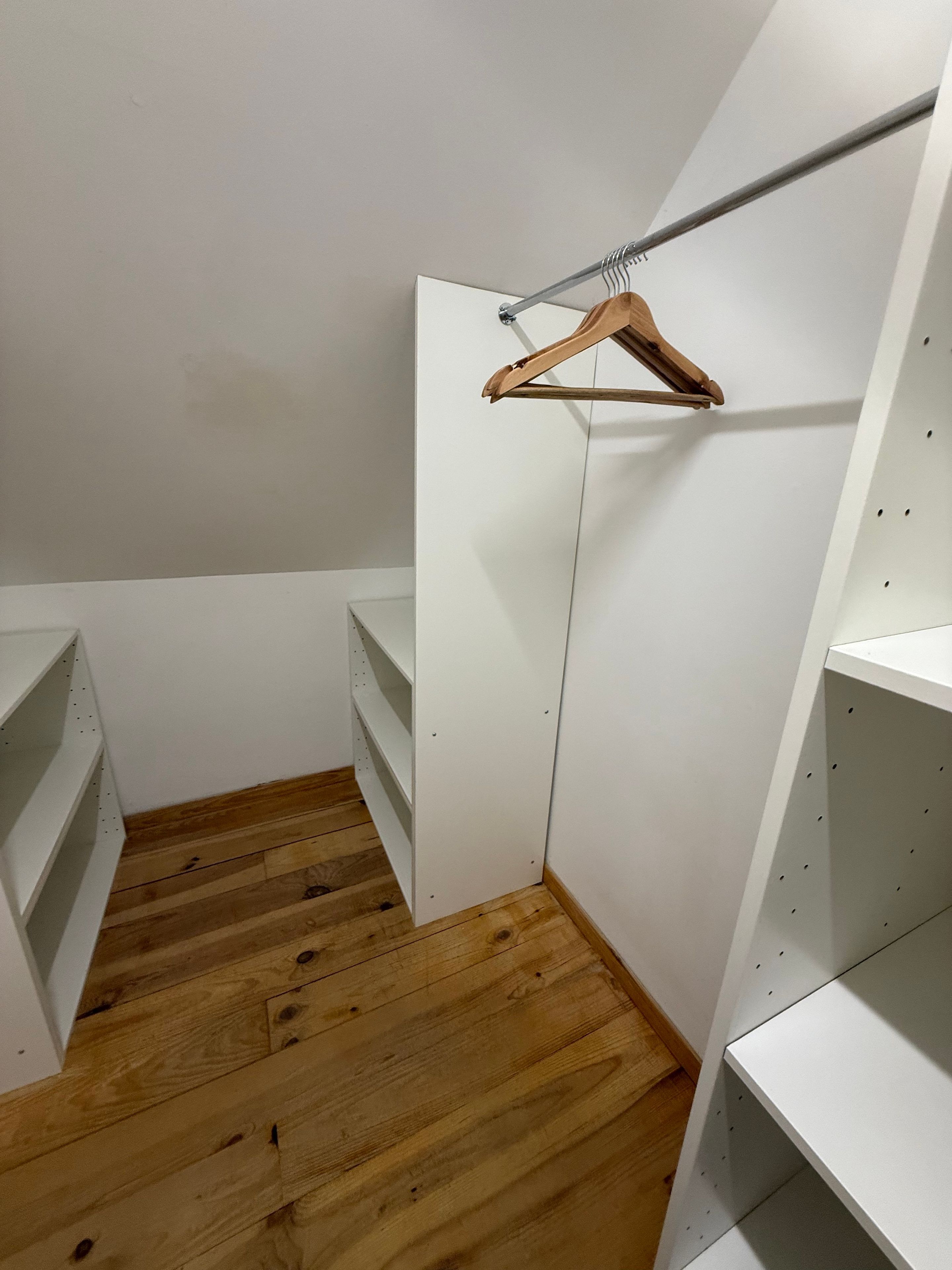 Un dressing accessible sans porte, doté d’un plancher en bois, d’étagères blanches et d’une tringle à vêtements en bois.