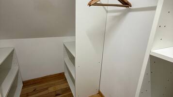 Un dressing accessible sans porte, doté d’un plancher en bois, d’étagères blanches et d’une tringle à vêtements en bois.