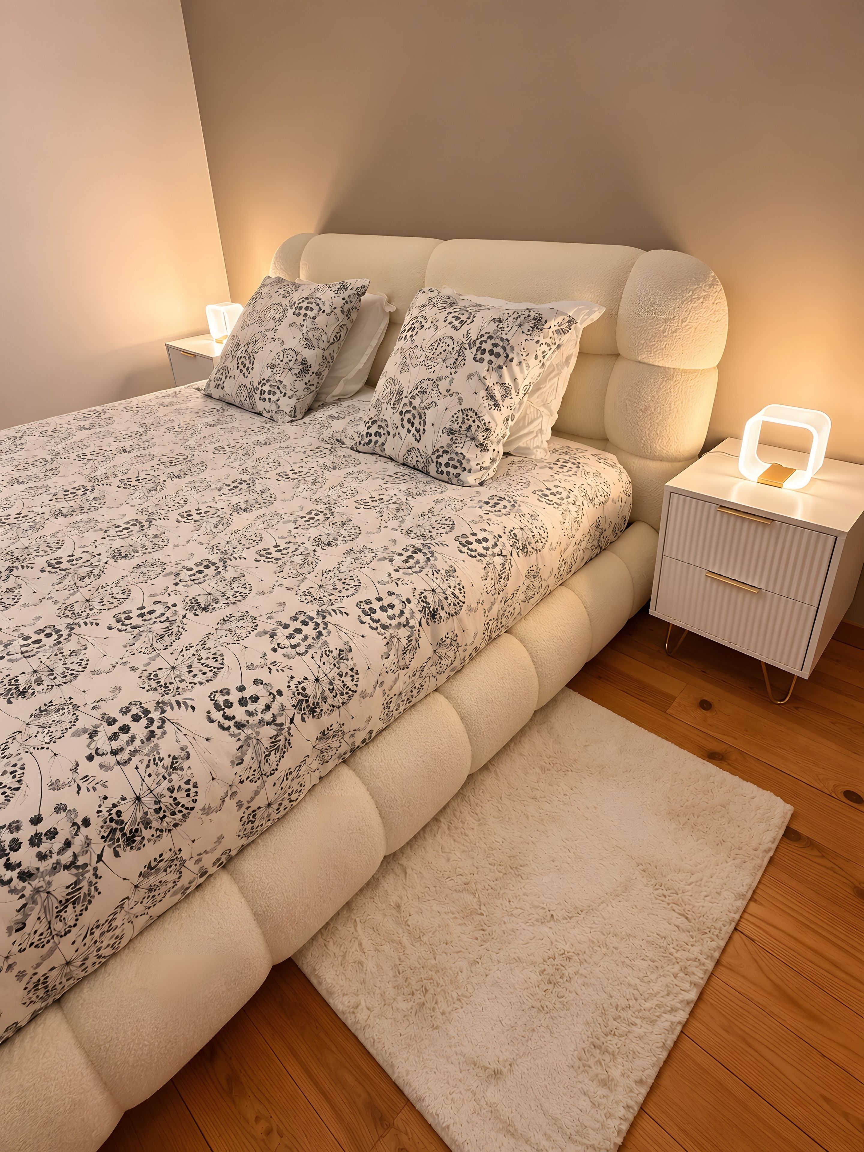 A bed with floral bedding, a bedside lamp, and a nightstand with a lamp.