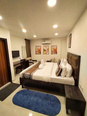 Una habitación de hotel con una cama, un escritorio, una silla, aire acondicionado y tres cuadros en la pared.