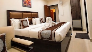 A hotel room with a large bed, a bedside table, a chair, a ceiling fan, and a painting on the wall. - Hotel SBS Plaza  (New Delhi)