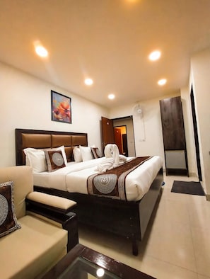 Una camera d'albergo con un letto grande, un comodino, una sedia, una ventola a soffitto e un quadro appeso al muro.