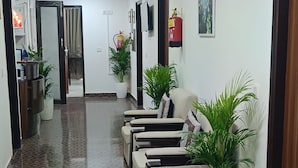 A reception area with a patterned floor, seating, potted plants, a fire extinguisher, and a television on the wall. - Hotel SBS Plaza  (New Delhi)
