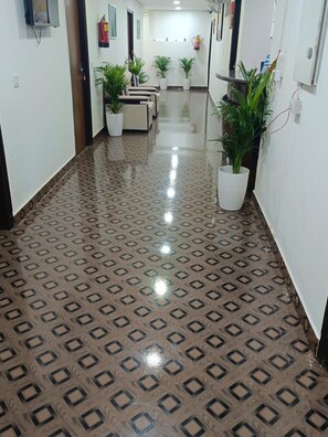 Un corridoio con pavimento decorato, piante in vaso e un estintore al muro.