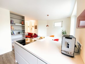 Eine moderne Küche mit einer zentralen Kochinsel, integrierten Regalen, einem roten Sofa und einem kleinen Fenster.