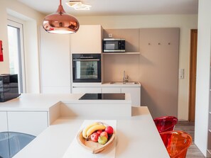 A modern kitchen with a central island, a microwave, oven, and a hanging pendant light. - Chesa Montana - Top 101 (Maria Alm am Steinernen Meer)
