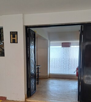 A hallway with a door labeled 'BLOCK H' leading to a room with a large window and a bamboo-patterned blind. - Cozy 1-bedroom apartment in serene Kiambu, Kenya with swimming pool (Kiambu)