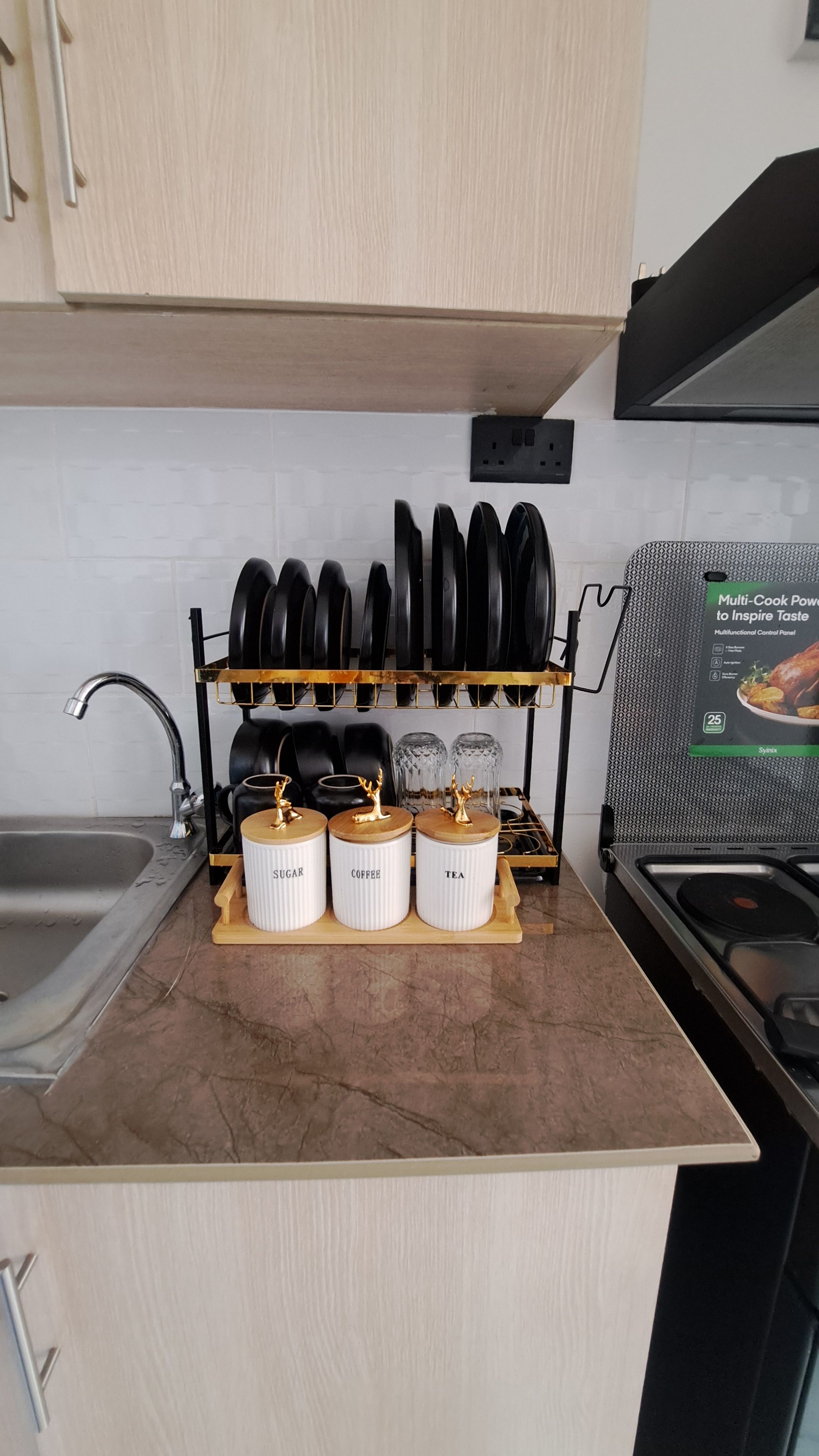 A kitchen with a countertop, a sink, a stove, a rack with pots, and jars labeled 'SUGAR,' 'COFFEE,' and 'TEA.'