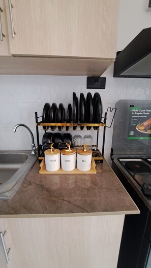 A kitchen with a countertop, a sink, a stove, a rack with pots, and jars labeled 'SUGAR,' 'COFFEE,' and 'TEA.' - Cozy 1-bedroom apartment in serene Kiambu, Kenya with swimming pool (Kiambu)