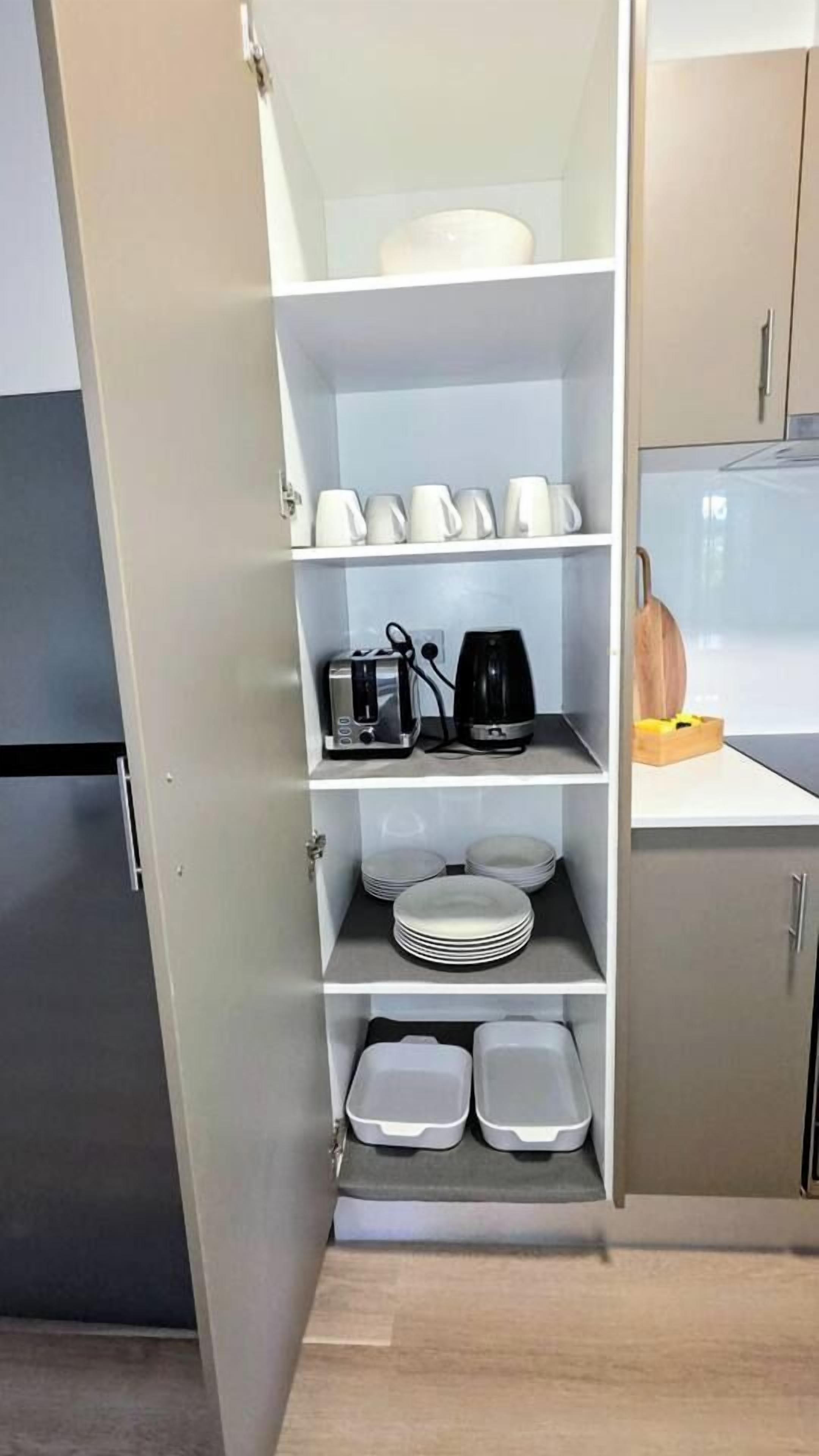 A kitchen with a built-in shelf unit containing kitchenware, a toaster, a coffee maker, and stacked plates.