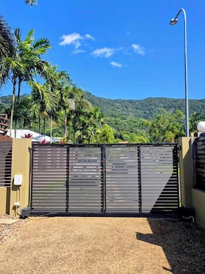 A gated entrance with a metal gate, a street lamp, and a view of a mountainous landscape with palm trees.
