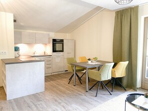 A compact kitchen with a central island, a dining area with two chairs, and a large window with curtains. - Chesa Montana - Top 204 (Maria Alm am Steinernen Meer)