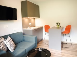 A modern living space with a sofa, a dining area with two chairs, a kitchen, and a flat-screen TV mounted on the wall. - Chesa Montana - Top 207 (Maria Alm am Steinernen Meer)