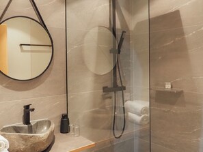 A modern bathroom with a stone sink, a round mirror, a handheld showerhead, and a glass-enclosed shower. - Chesa Montana - Top 206 (Maria Alm am Steinernen Meer)