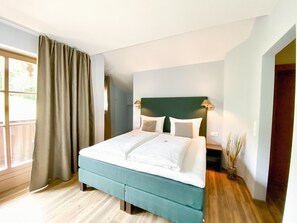 A hotel room with a bed, curtains, a nightstand, a lamp, and a view of the outdoors. - Chesa Montana - Top 206 (Maria Alm am Steinernen Meer)