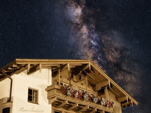 A building with a balcony adorned with flowers, under a starry night sky. - Chesa Montana - Top 206 (Maria Alm am Steinernen Meer)