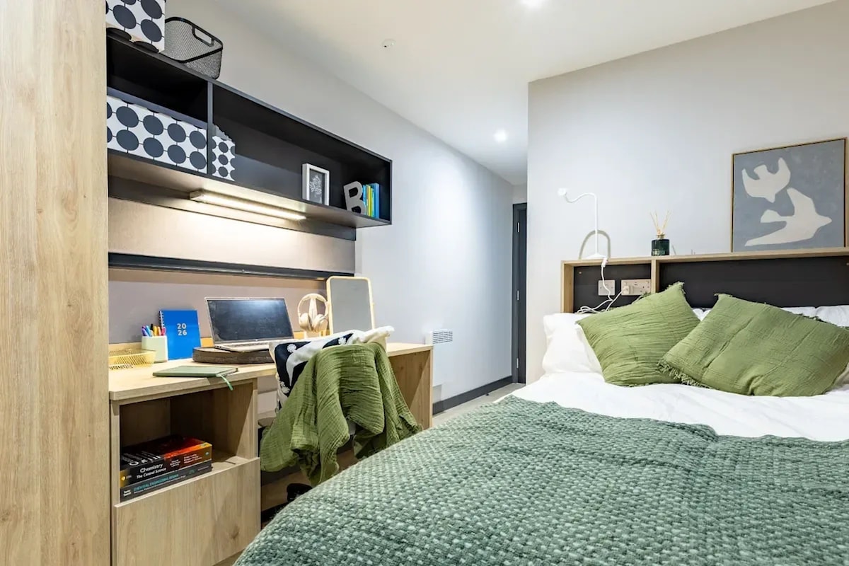Ein modernes Schlafzimmer mit einem Bett, einem Schreibtisch mit einem Laptop, Regalen mit Büchern und einer Wandlampe.