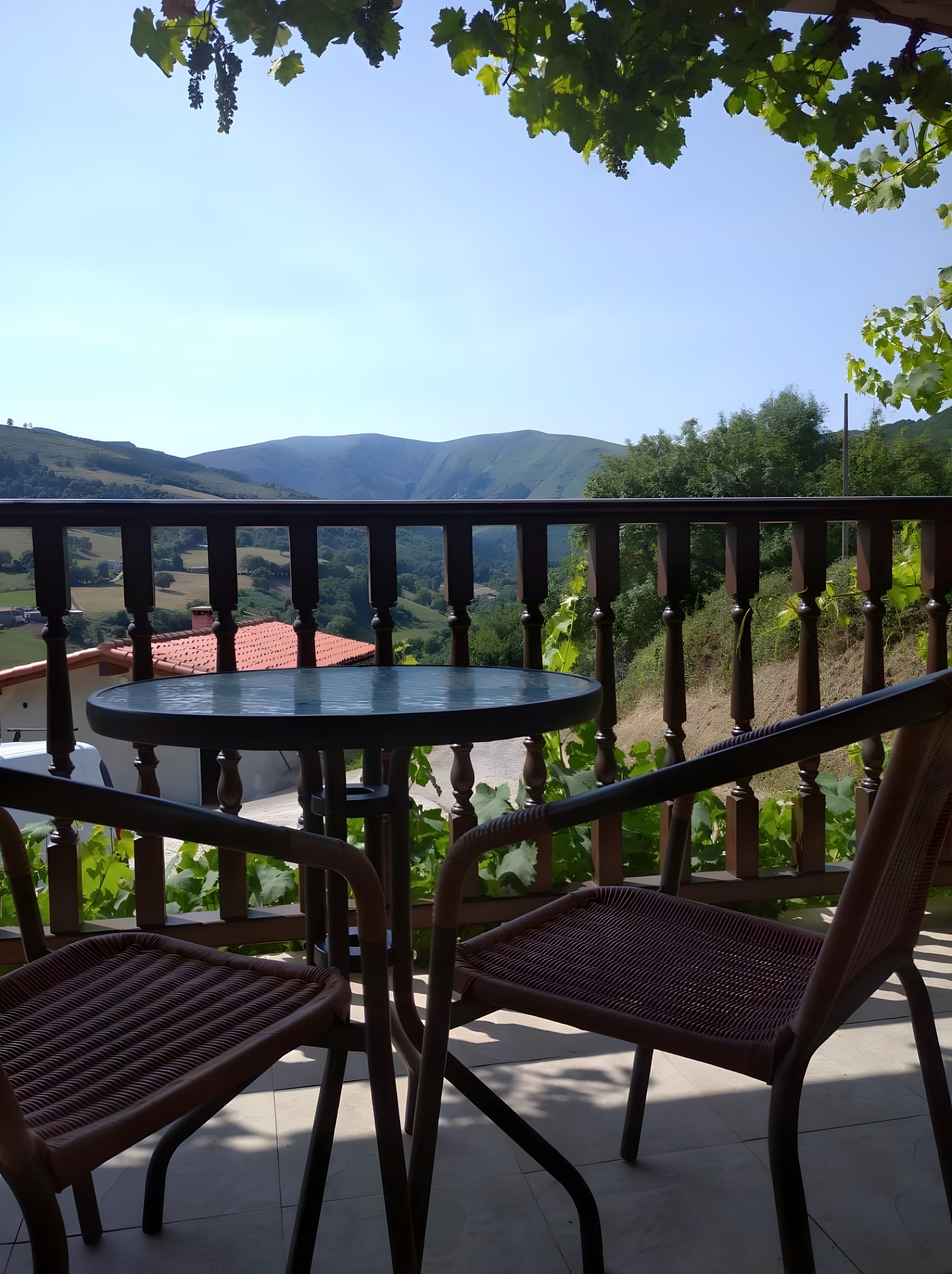 Un balcón con mesa y sillas, con vista a un paisaje montañoso.